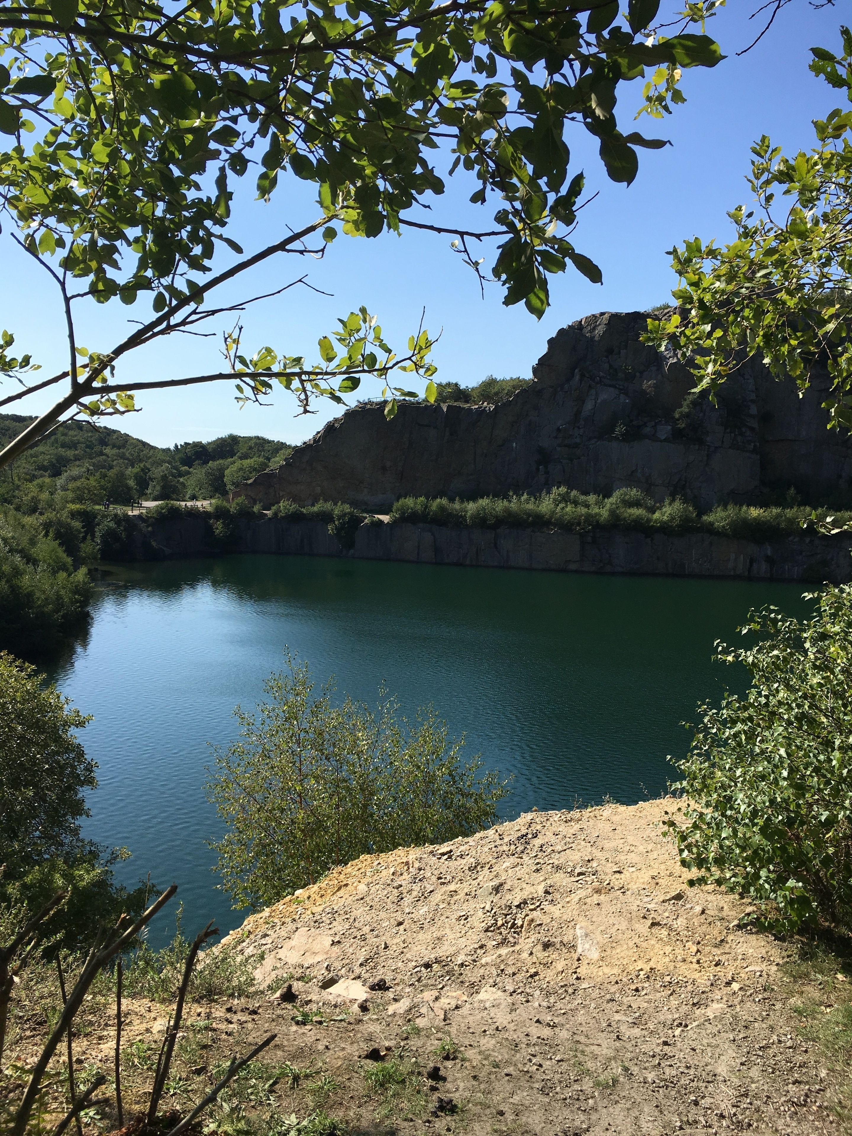 A natural landscape with a calm lake, rocky cliffs, and dense greenery.