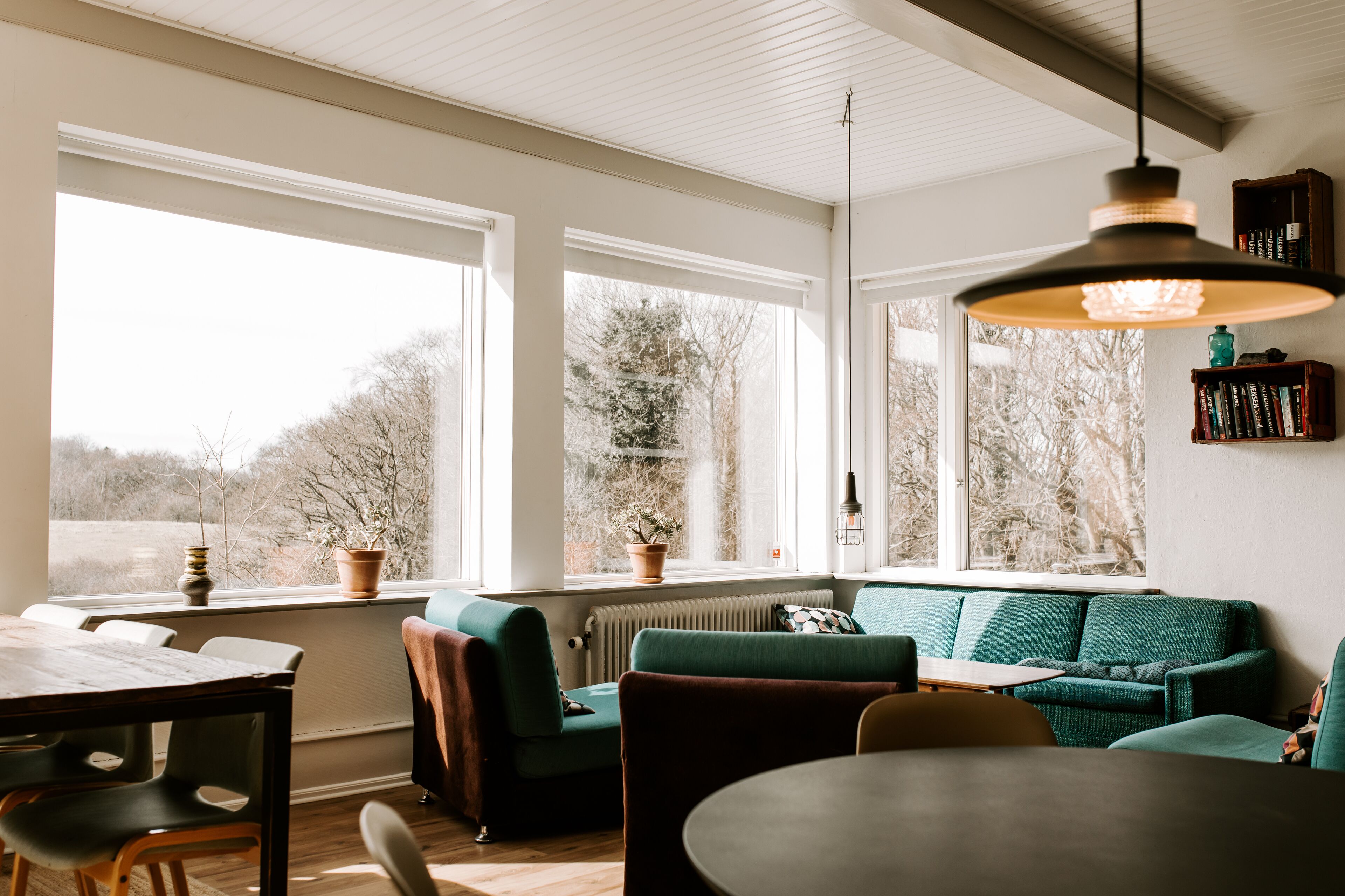A cozy living room with a green sofa, a dining table, and a large window providing a view of trees.