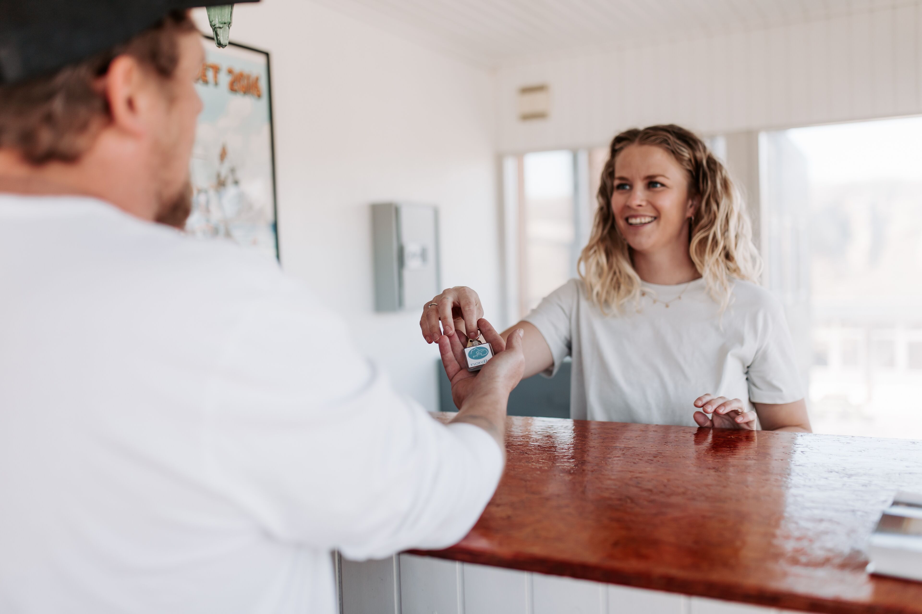 Une personne remet une clé à une autre personne au comptoir, dont la surface est en bois.