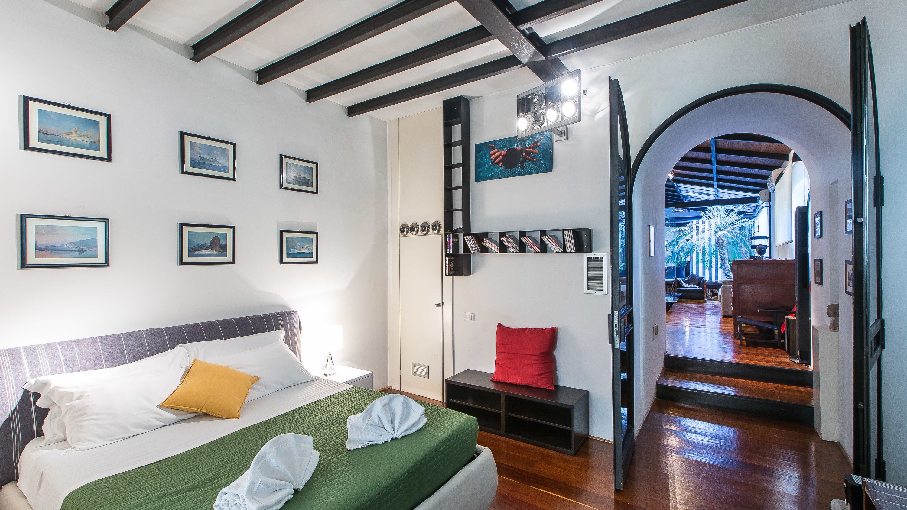 A hotel room with a bed, a bookshelf, and a view of the hallway.
