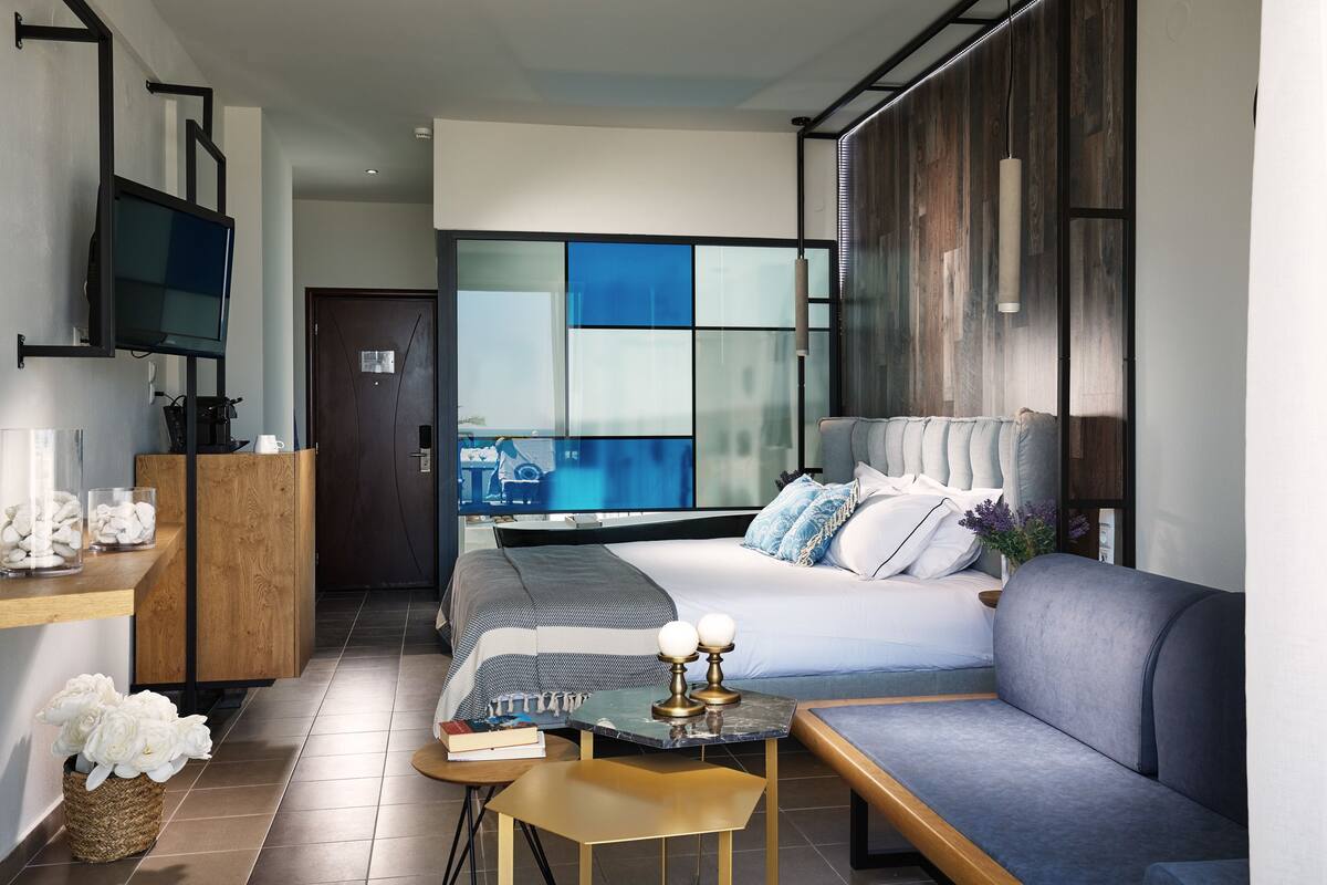 Quarto de hotel moderno com uma cama grande, um sofá, uma mesa pequena e uma televisão na parede.
