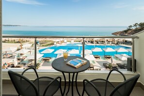 Ein Balkon mit Blick auf Pool und Strand. Liegestühle und Sonnenschirme sind vorhanden.