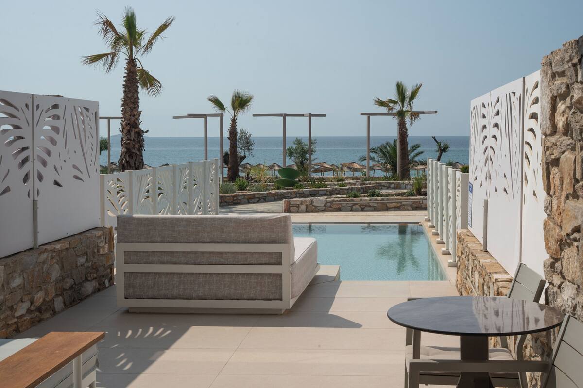 Área à beira da piscina com sofá, mesa e vista para o mar.