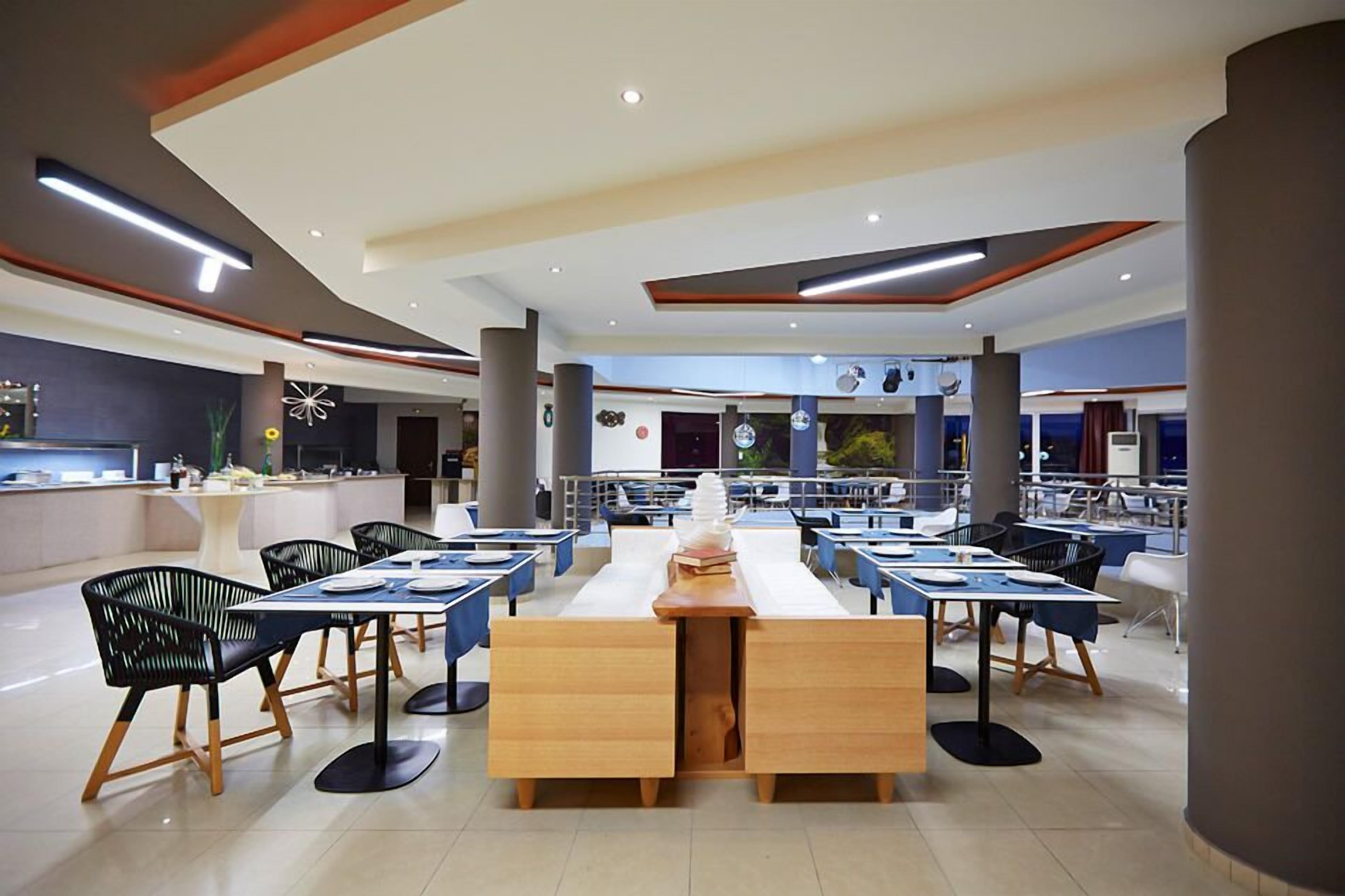A modern dining area with long tables and black chairs, featuring a central wooden table with a stack of books and a vase.