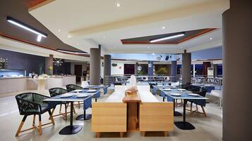 A modern dining area with long tables and black chairs, featuring a central wooden table with a stack of books and a vase.