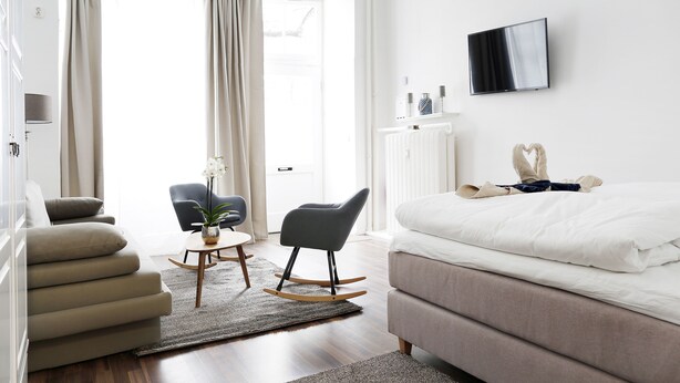 A modern hotel room with a large bed, a TV mounted on the wall, and a seating area with a chair and a small table. - DROY Droysenstr. Old building - box spring beds - near Kurfürstendamm (Berlin)