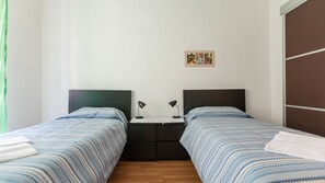 Ein Doppelzimmer mit zwei Betten, einem Nachttisch, einem kleinen Tisch und einem an der Wand hängenden Bild.