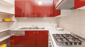 Una cocina compacta con gabinetes rojos, un lavamanos de acero inoxidable, una estufa a gas y un tazón amarillo en un estante.