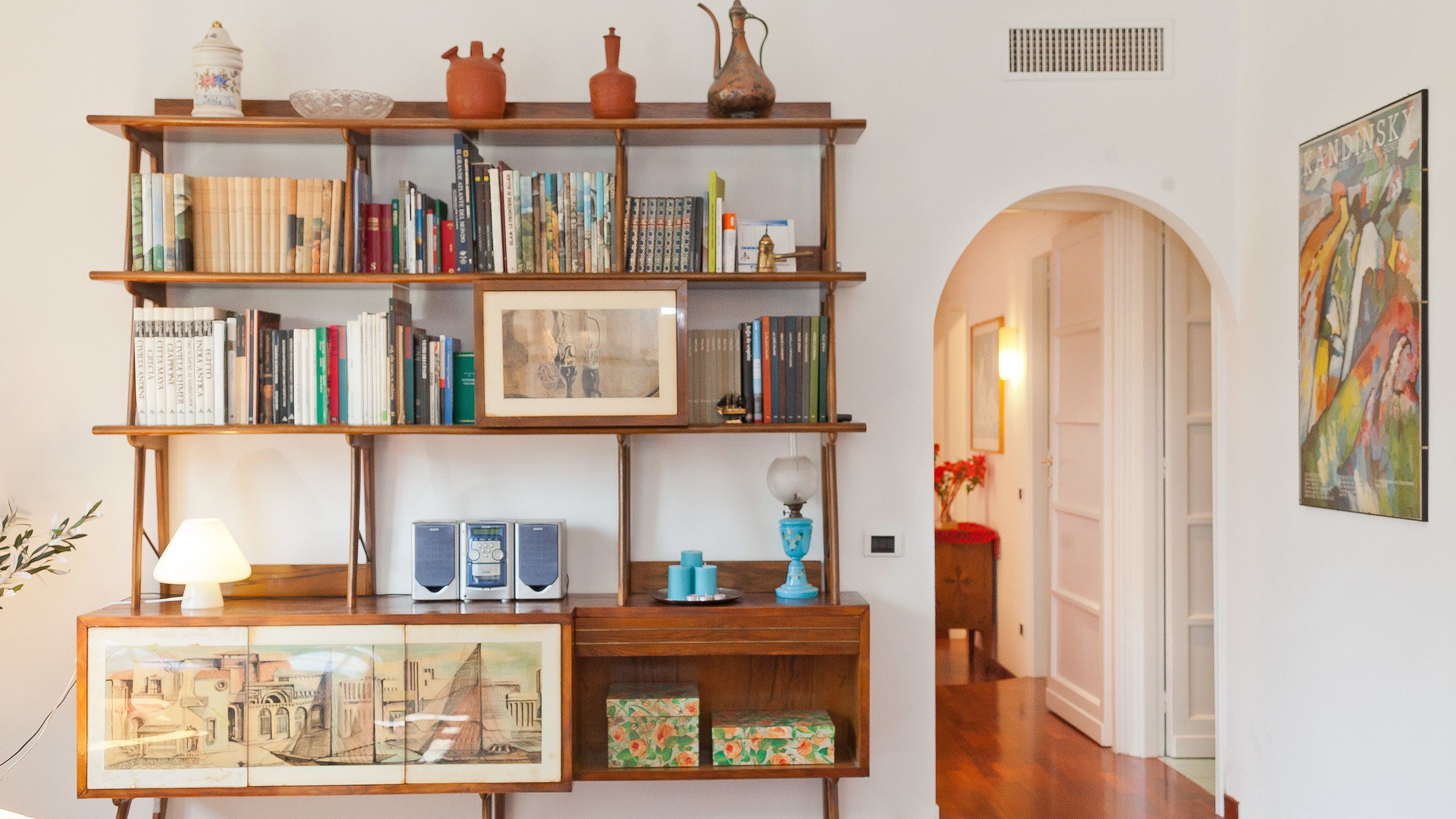 A bookshelf with books and decorative items, a framed picture, and a small table with a lamp and speakers.