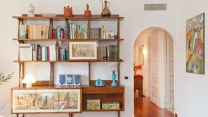A bookshelf with books and decorative items, a framed picture, and a small table with a lamp and speakers. - Rental In Rome Pateras Flower (Rome)