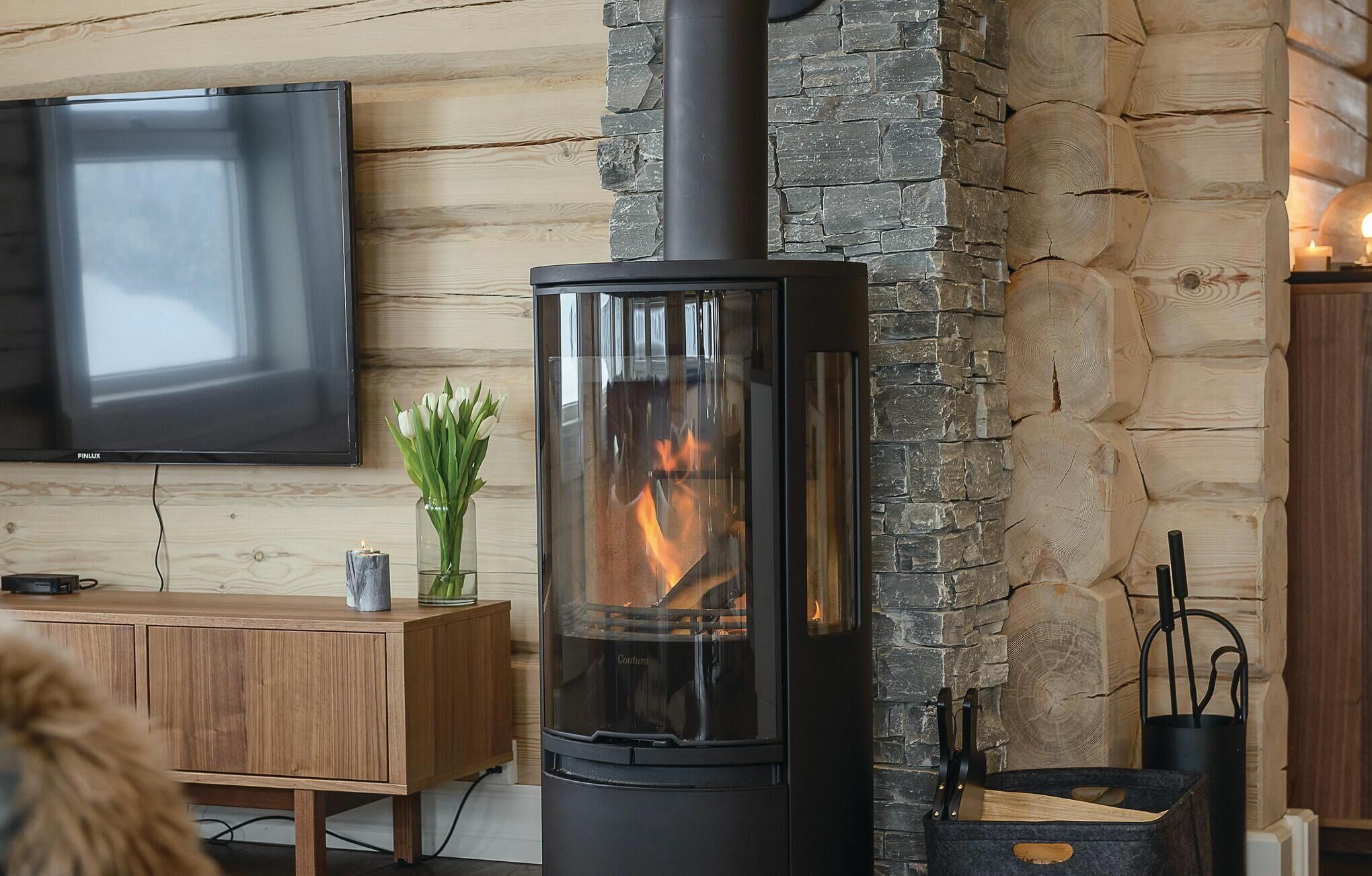A modern living room with a stone wall, a black wood-burning stove, a wooden cabinet, and a TV mounted on the wall.