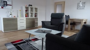 A modern living room with a white cabinet, a black armchair, a small table, and a wooden desk.