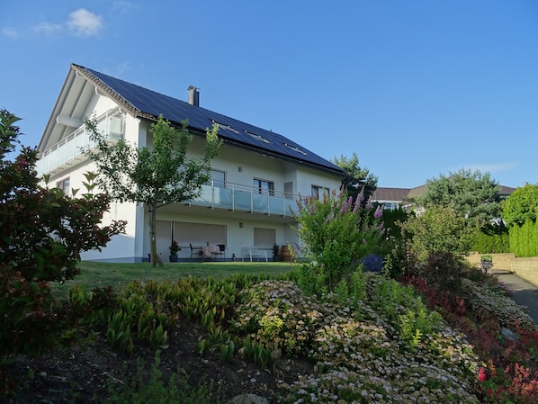 A two-story house with a balcony, solar panels, and a well-maintained garden.