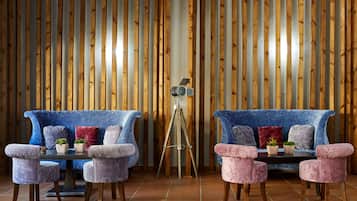 A room with two sofas and two armchairs, a tripod, and a small table with potted plants.