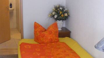 A small, neatly arranged bedroom with a bed, pillows, a nightstand, and a vase of flowers.