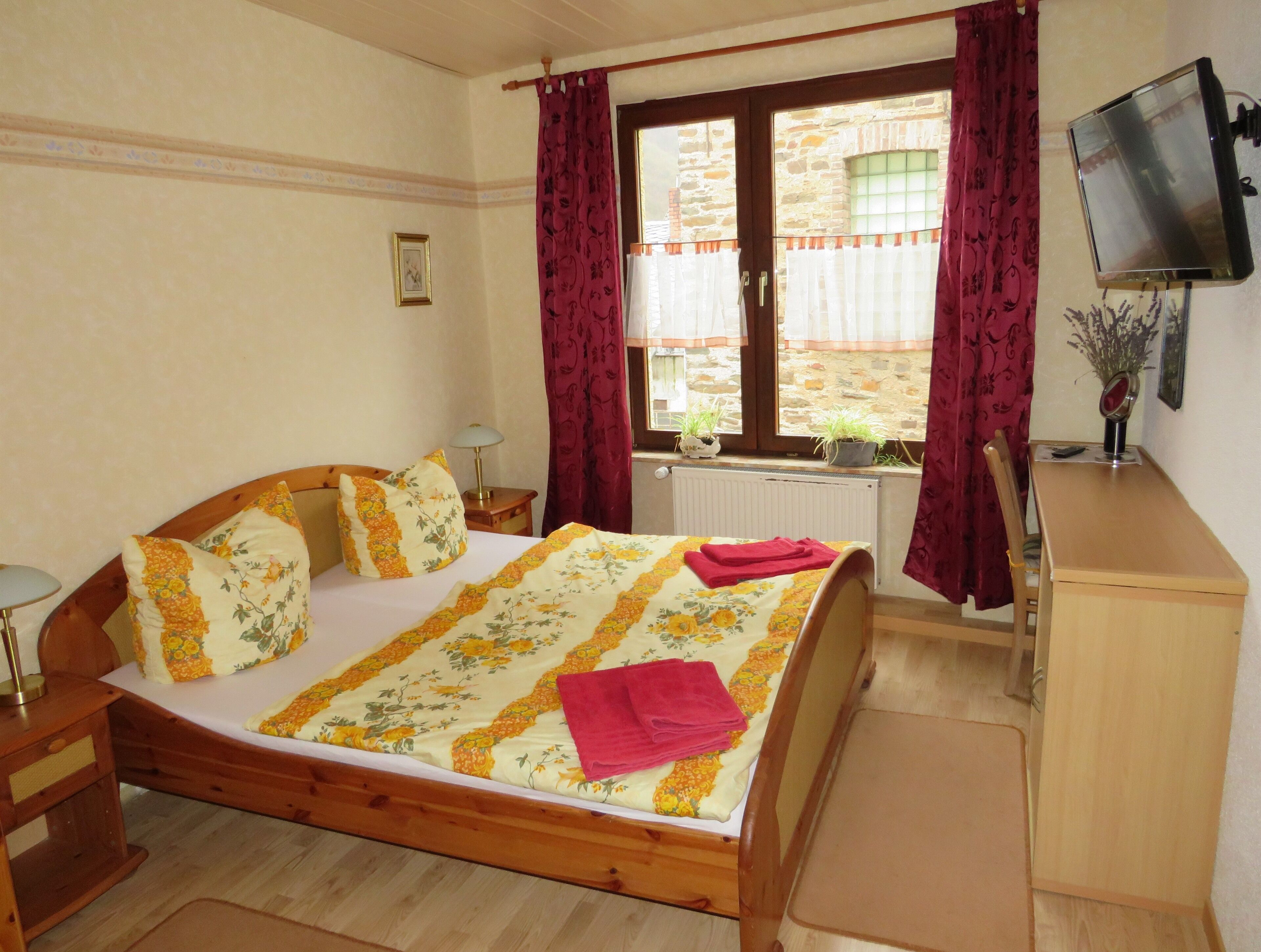 A bedroom with a wooden bed, a desk, a television, and a window with curtains.