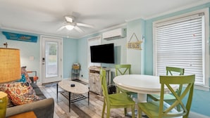 A dining area with a white table and green chairs, a ceiling fan, and a television on the wall. - Short Walk to Shops, Restaurants & Beach Access,Pet Friendly, Private fenced in yard (Folly Beach)