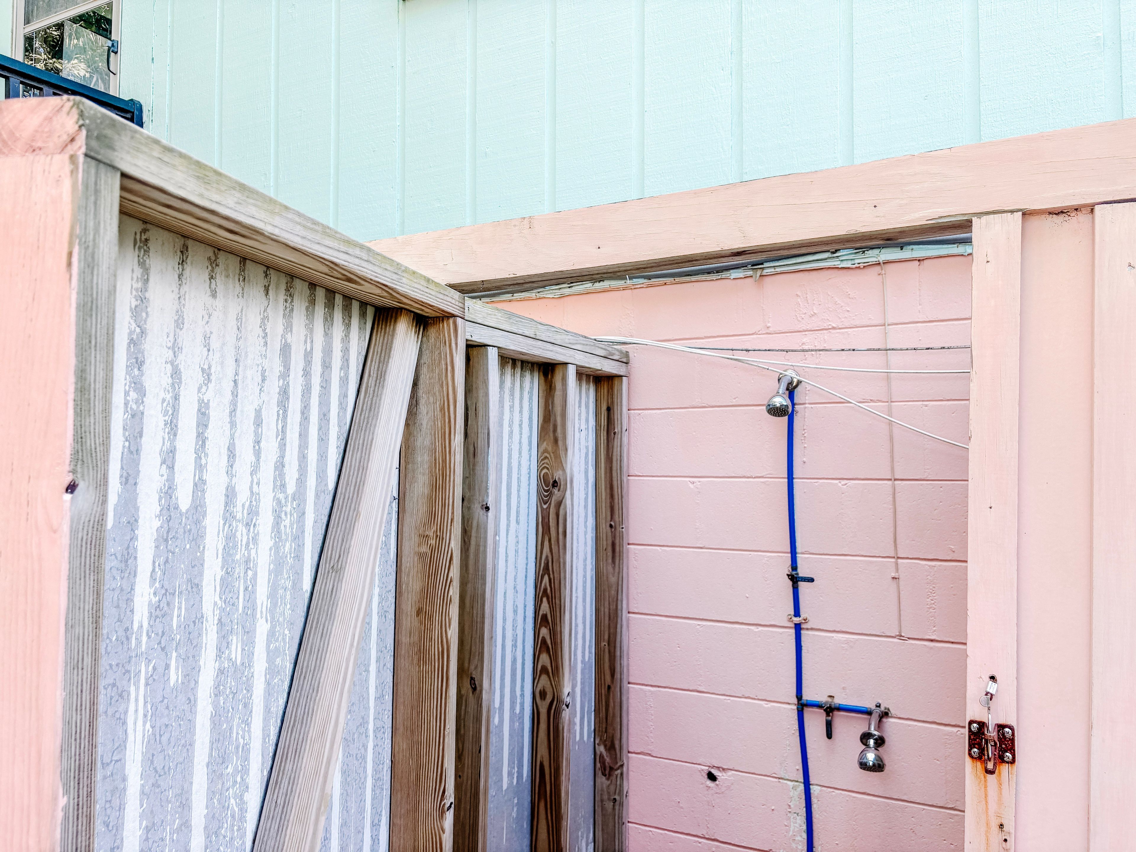 A wooden door with a metal latch, a pink wall with a blue hose, and a metal pipe.