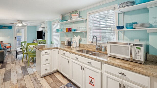 A kitchen with white cabinets, a granite countertop, and a microwave. There are shelves above the counter holding dishes and glasses. - Short Walk to Shops, Restaurants & Beach Access,Pet Friendly, Private fenced in yard (Folly Beach)