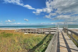 A wooden boardwalk leading to a beach with a clear view of the ocean and a cloudy sky.