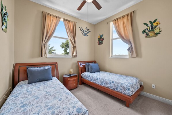 A bedroom with two single beds, beige walls, and a ceiling fan.