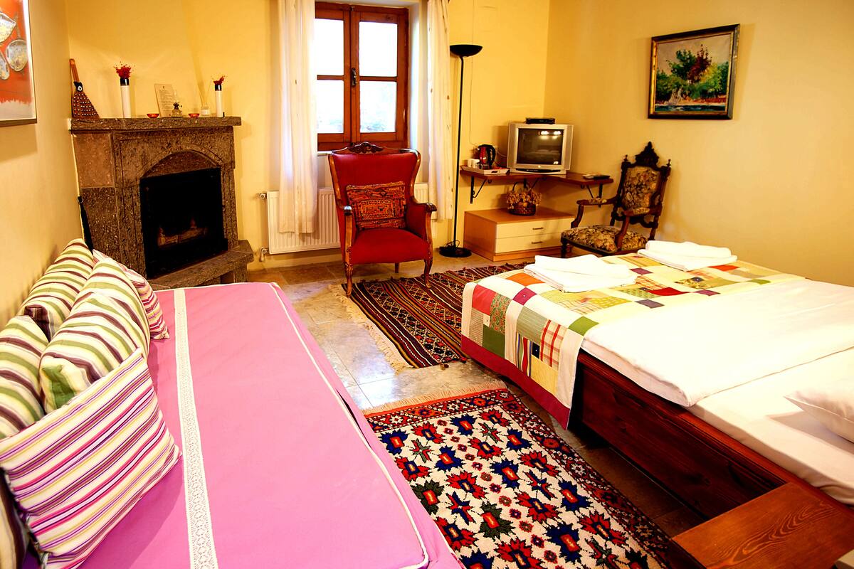 Un dormitorio acogedor con chimenea, una cama con colcha colorida, una silla y un televisor.