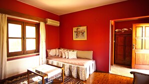 Una habitación con una pared roja, un banco de madera con cojines, una mesa con mantel, un radiador y una puerta.