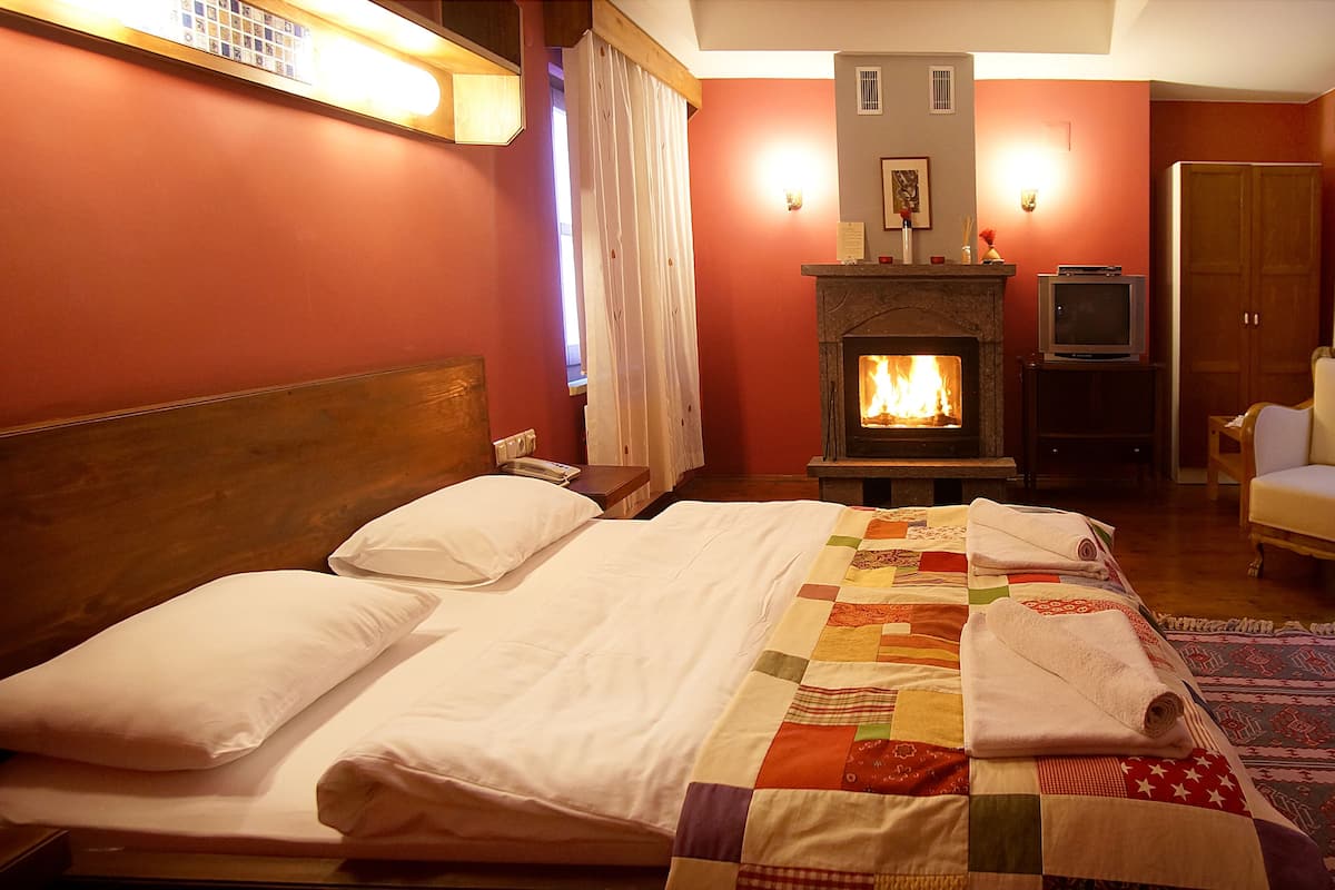 Una habitación de hotel con una cama, chimenea, televisor y una silla.