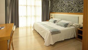 A hotel room with a bed, a wooden desk, and a window with curtains.