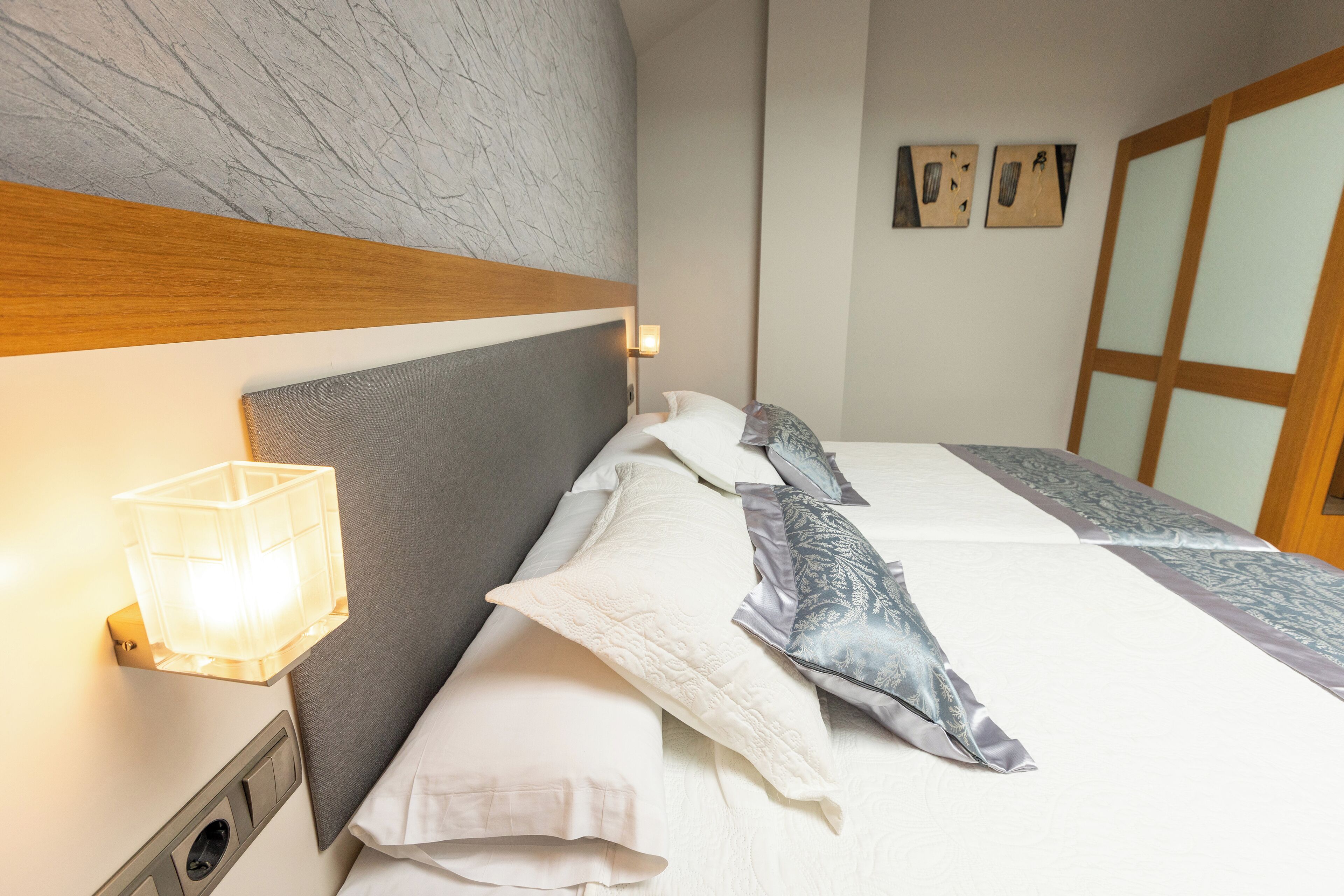A neatly made bed with a headboard, a bedside lamp, and a wall-mounted light.