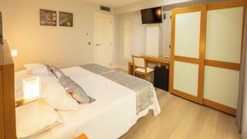 A hotel room with a bed, desk, chair, TV, wardrobe, and artwork on the wall.