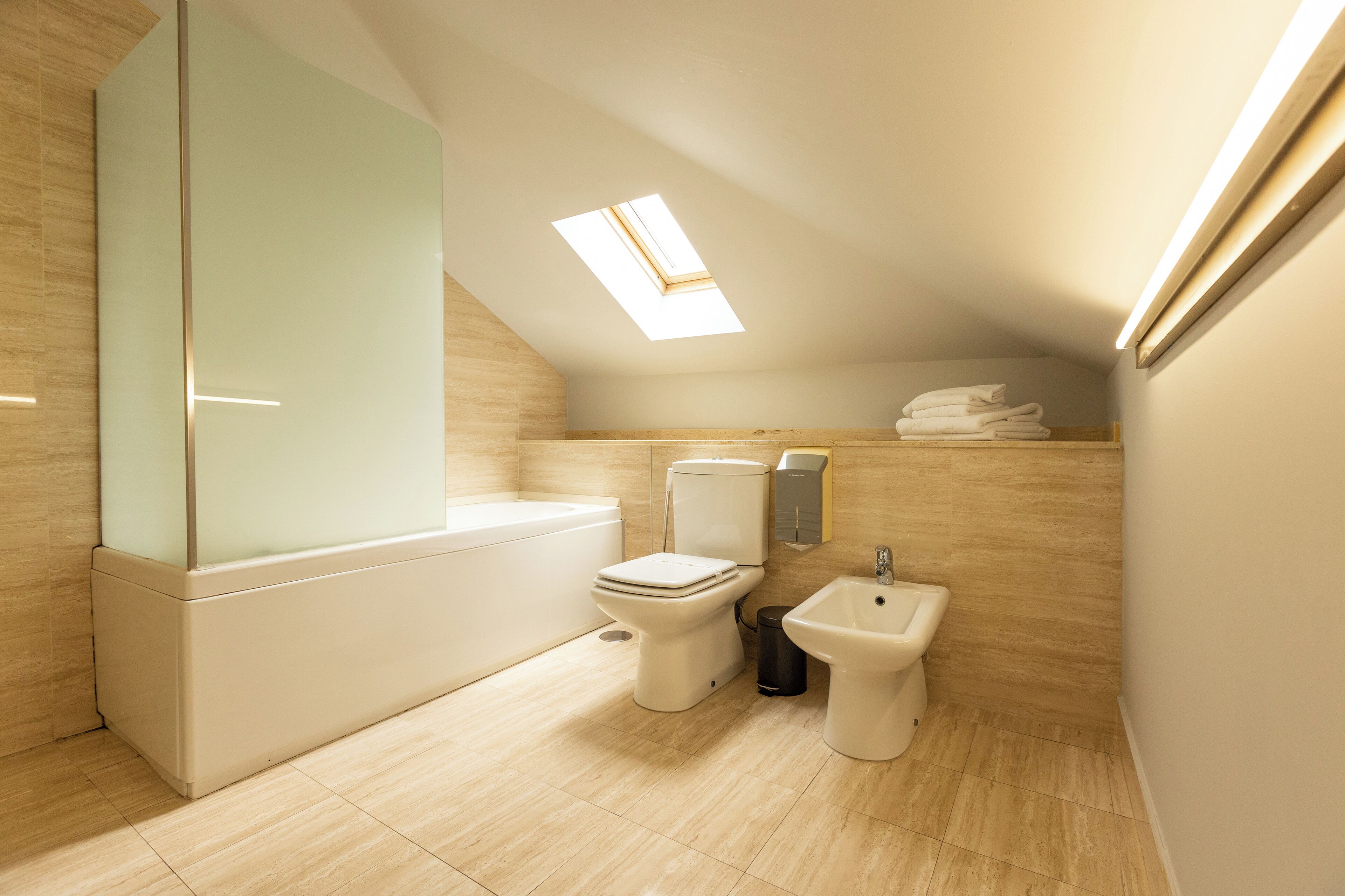 Een moderne badkamer met dakraam, een badkuip, toilet, bidet en spiegel.