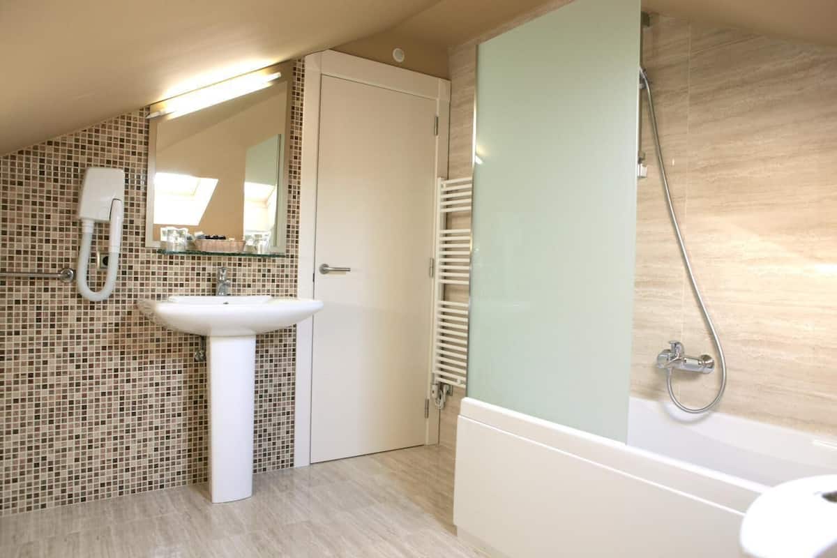 A bathroom with a tiled wall, a sink, a mirror, a shower, and a door.