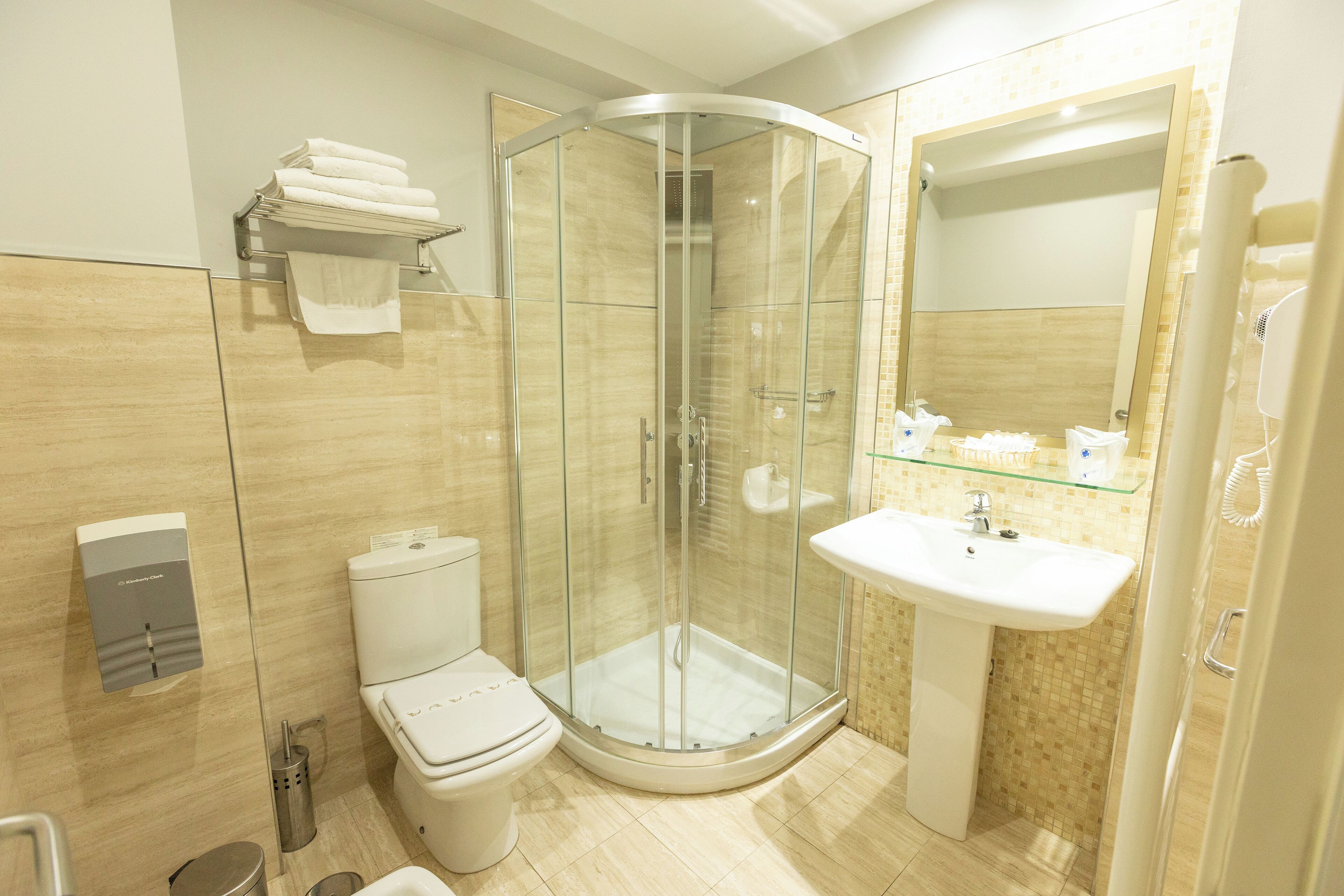 Ein modernes Badezimmer mit Duschkabine aus Glas, Toilette, Waschbecken und einem Handtuchhalter mit gefalteten Handtüchern.