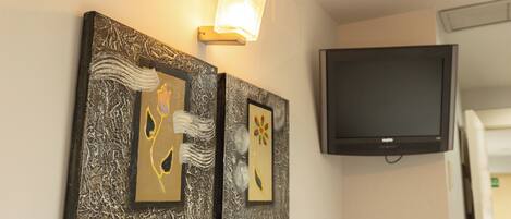 Two framed artworks on a wall, a flat-screen TV mounted above them, and a door to the right.