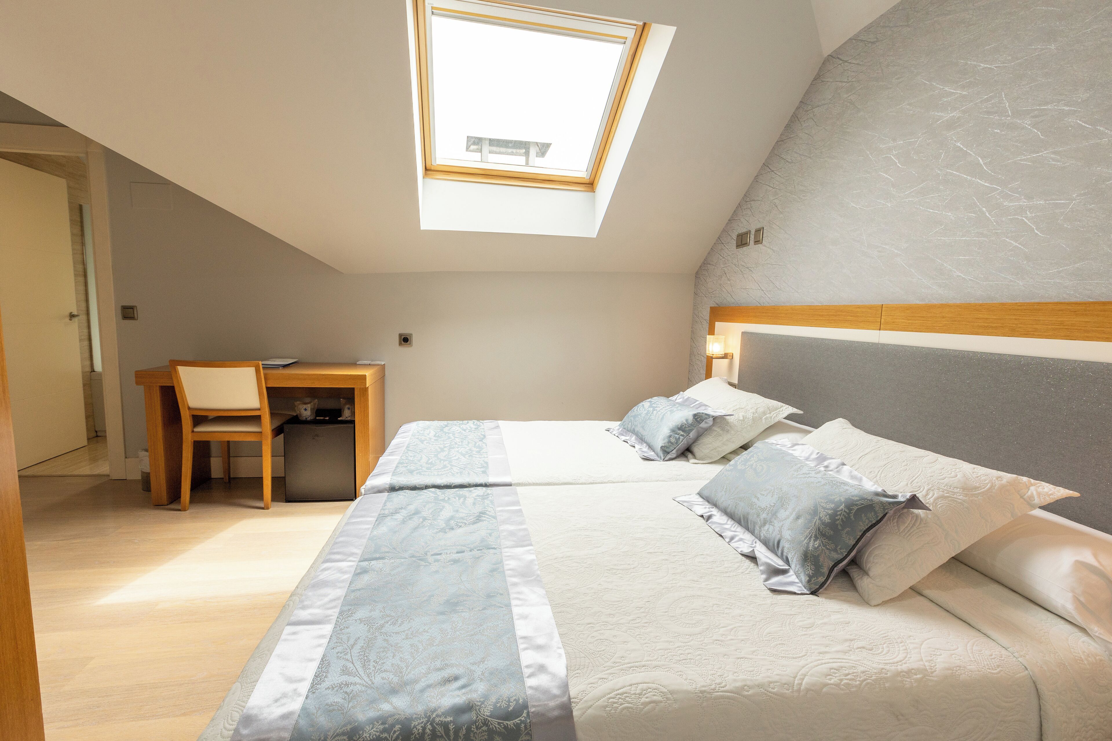 Ein Schlafzimmer mit Oberlicht, einem Bett mit Kissen, einem Schreibtisch und einem Stuhl.