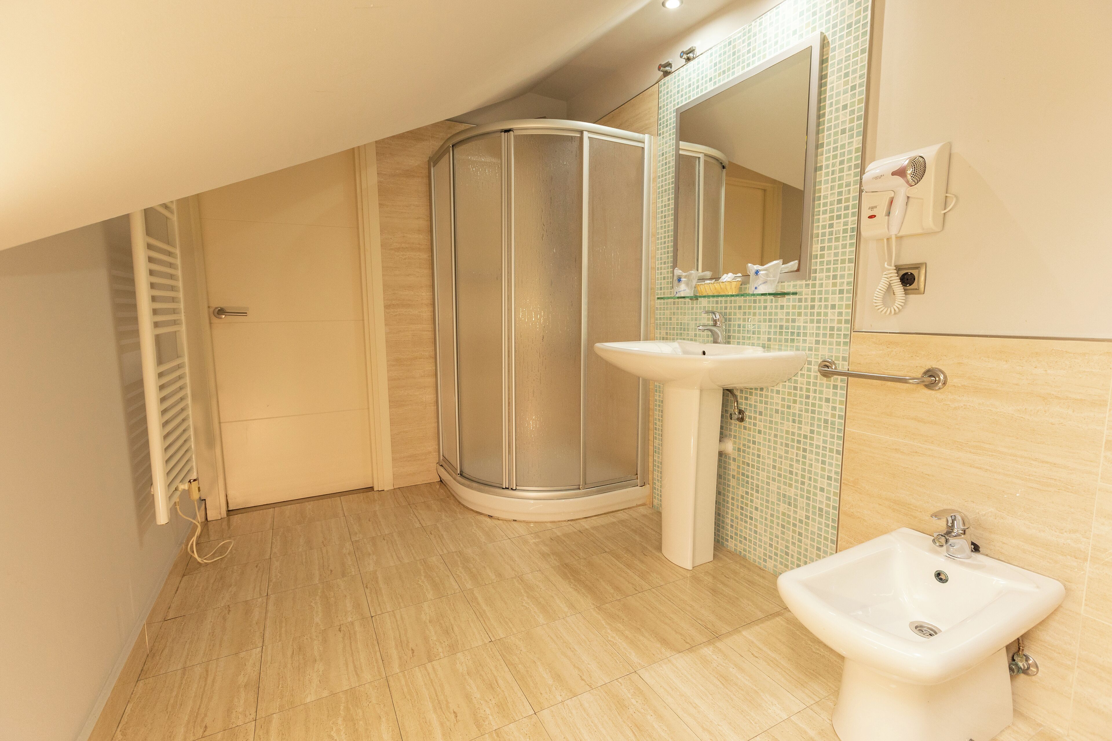 Un baño moderno con ducha, lavamanos y secador de pelo montado en la pared.