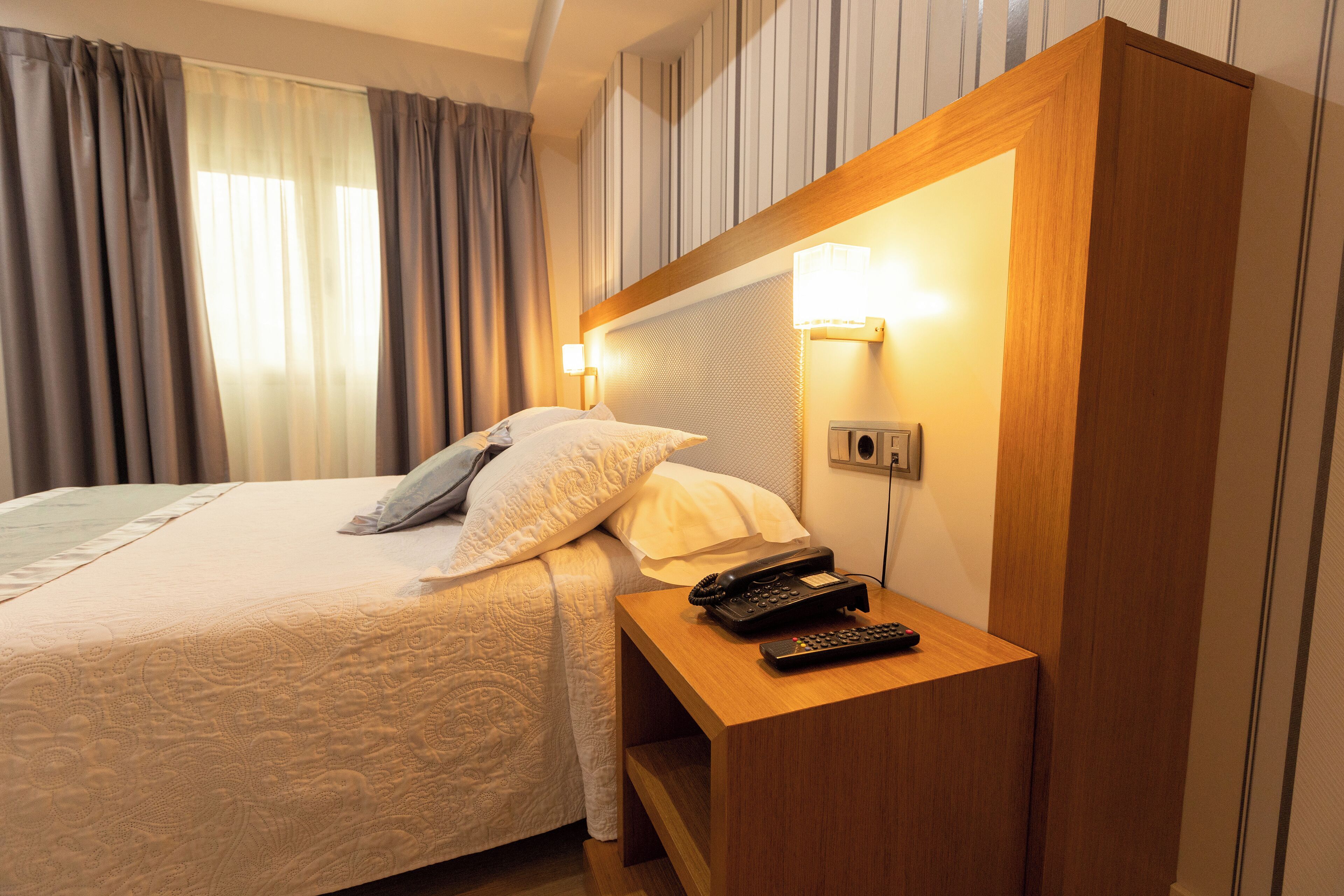 A hotel room with a bed, a bedside table with a phone, and a wall-mounted light.