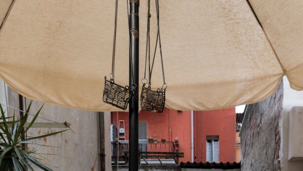 A round table with a green bowl, a white chair, and a hanging basket under an umbrella. - Get the local feel in a nice and safe neighborhood in the heart of Rome! (rome)