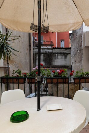 Una mesa redonda con un bol verde, una silla blanca y una cesta colgante bajo un paraguas.