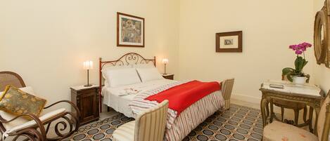 A neatly arranged bedroom with a bed, two bedside tables, a chair, a small table, and a potted plant.