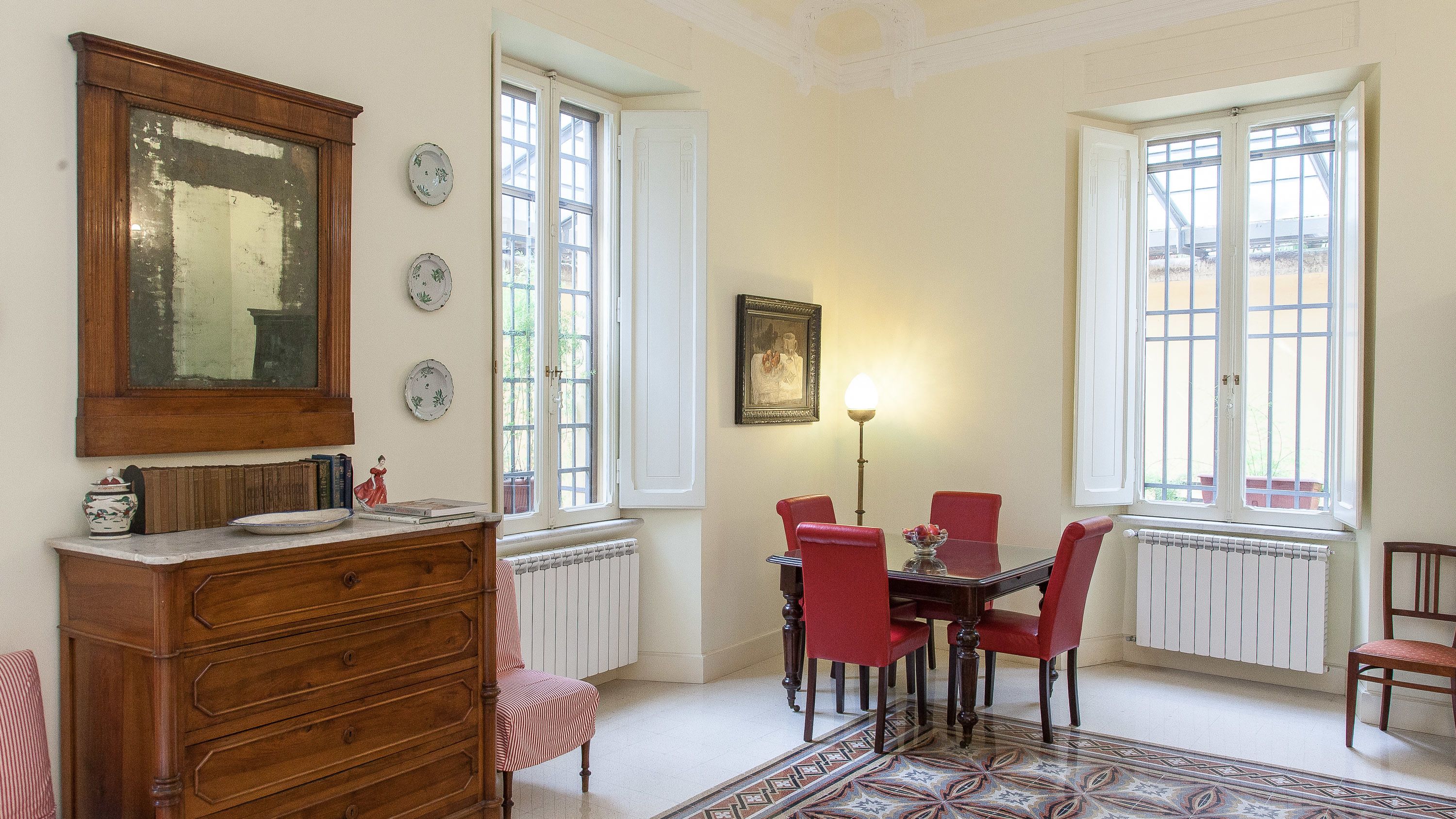 Une salle à manger avec une table en bois, des chaises rouges, un tapis à motifs et un grand miroir au-dessus de la commode.