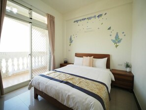 Habitación de hotel con cama, mesita de noche, planta en maceta y vista a un balcón.