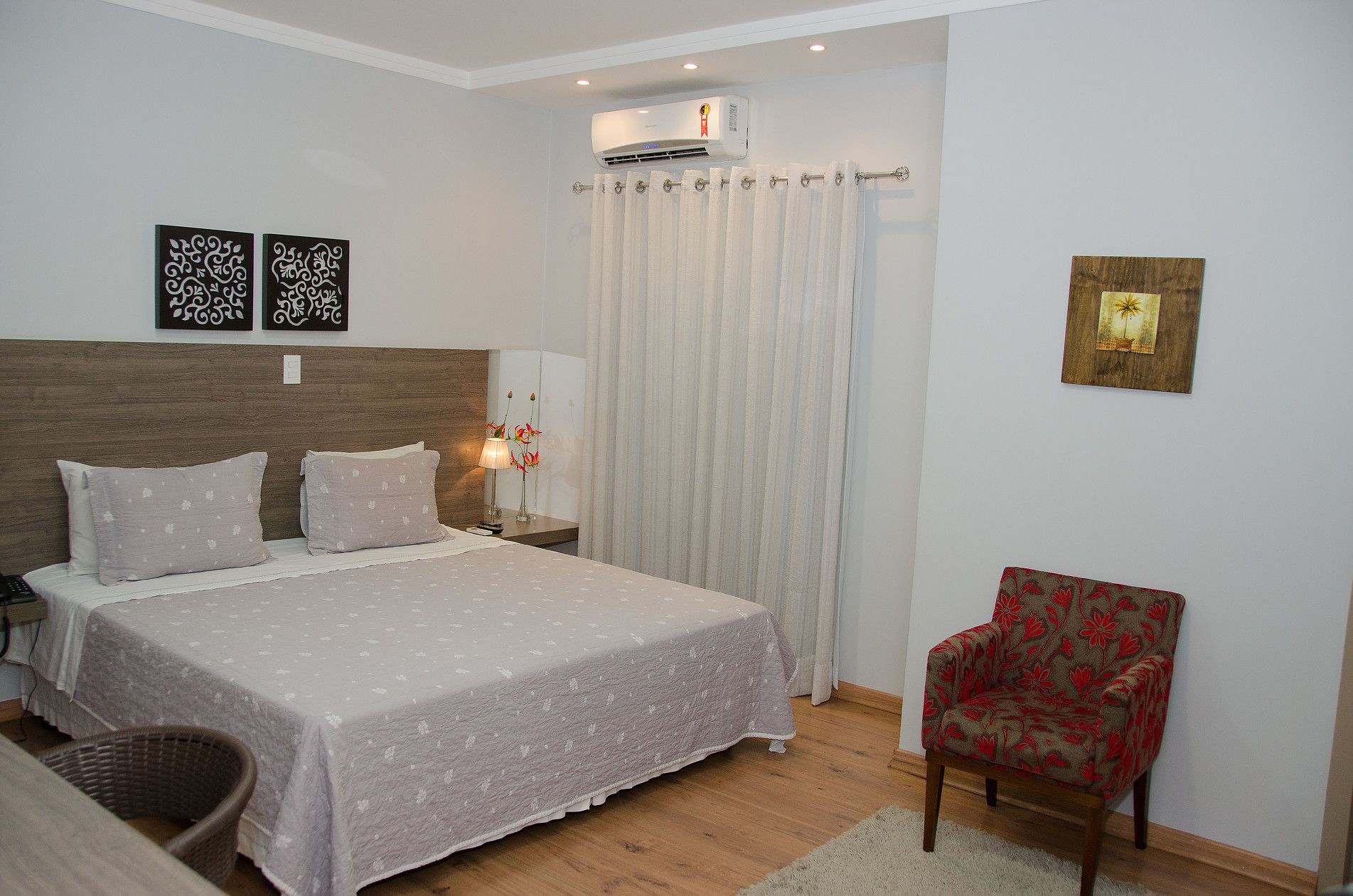A bedroom with a bed, nightstand, lamp, chair, and decorative wall art.