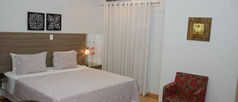A bedroom with a bed, nightstand, lamp, chair, and decorative wall art.