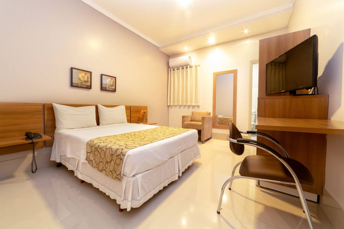 A hotel room with a bed, a desk, a chair, a phone, a TV, and a mirror.