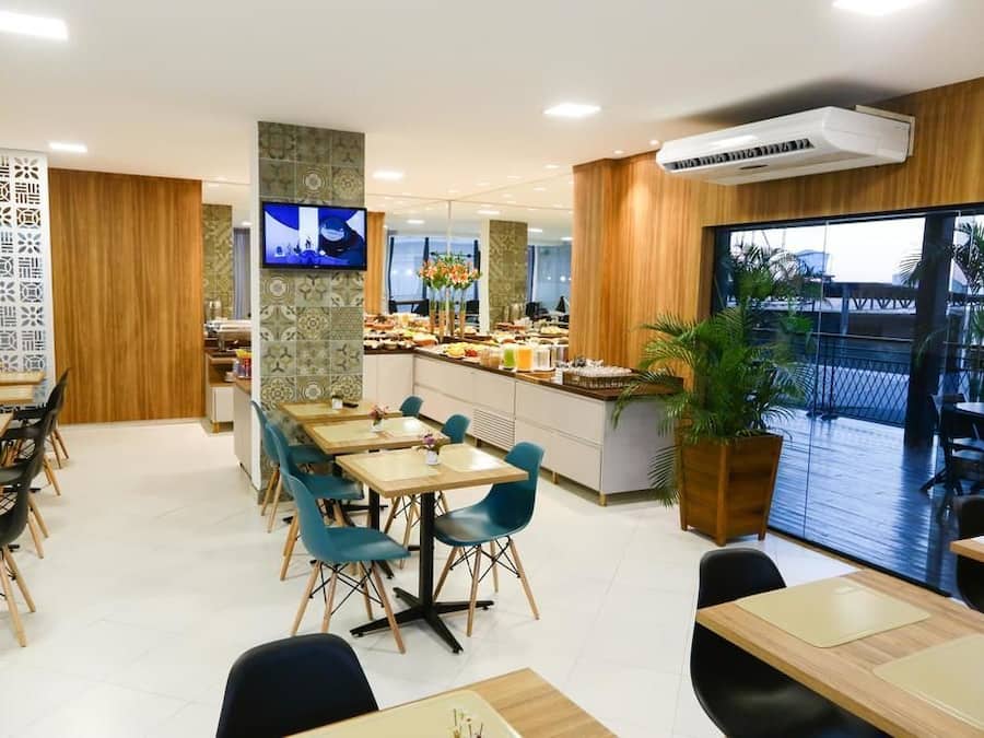 A modern dining area with wooden tables and chairs, a buffet counter, and a large window offering a view of the outdoors.