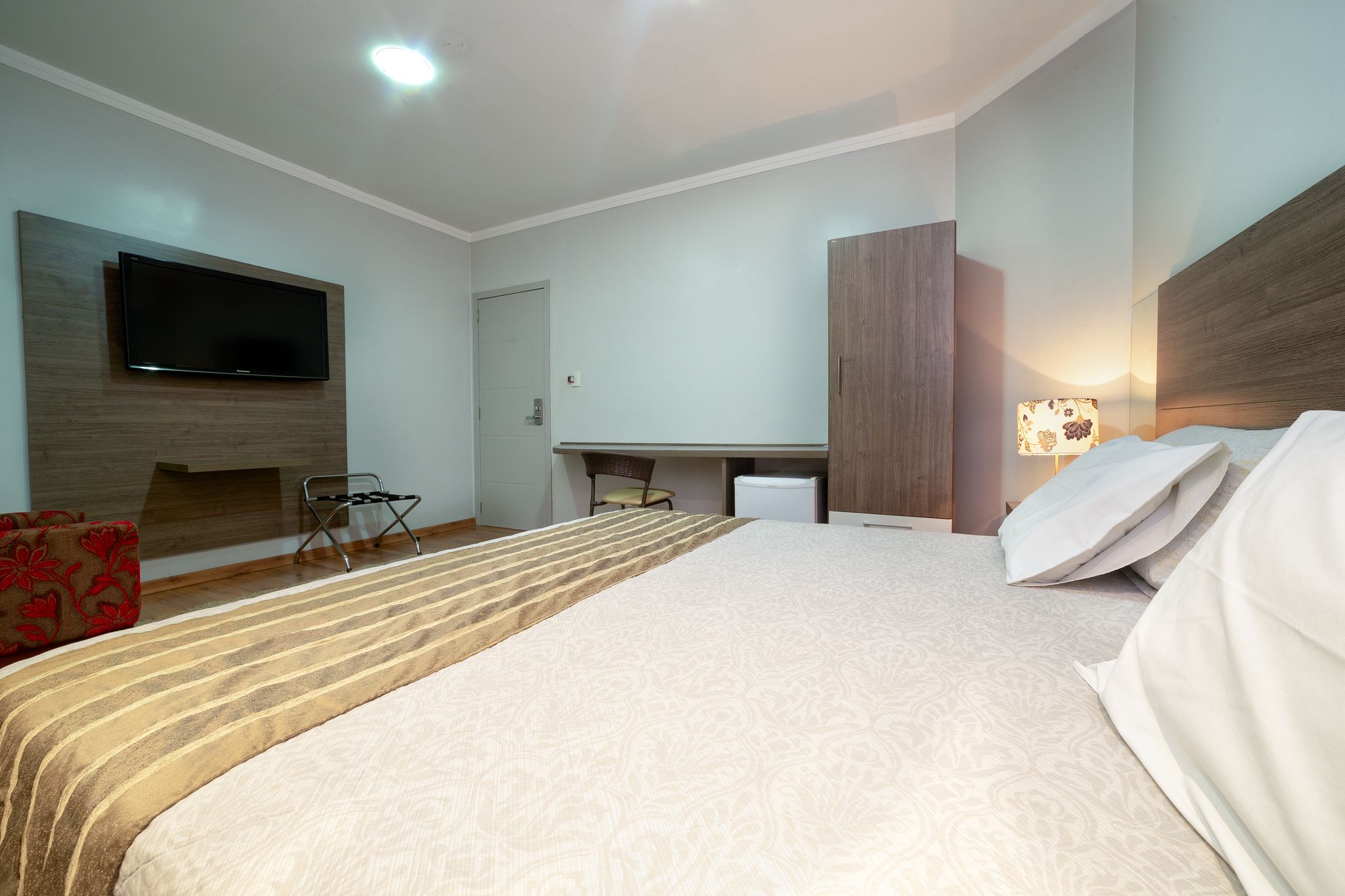Een hotelkamer met een bed, een aan de muur bevestigde televisie, een bureau en een stoel.