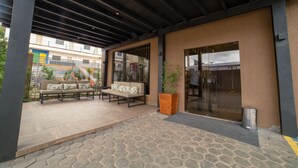 Un área de estar al aire libre con un banco de madera y un sofá, una planta en maceta y una puerta de vidrio.