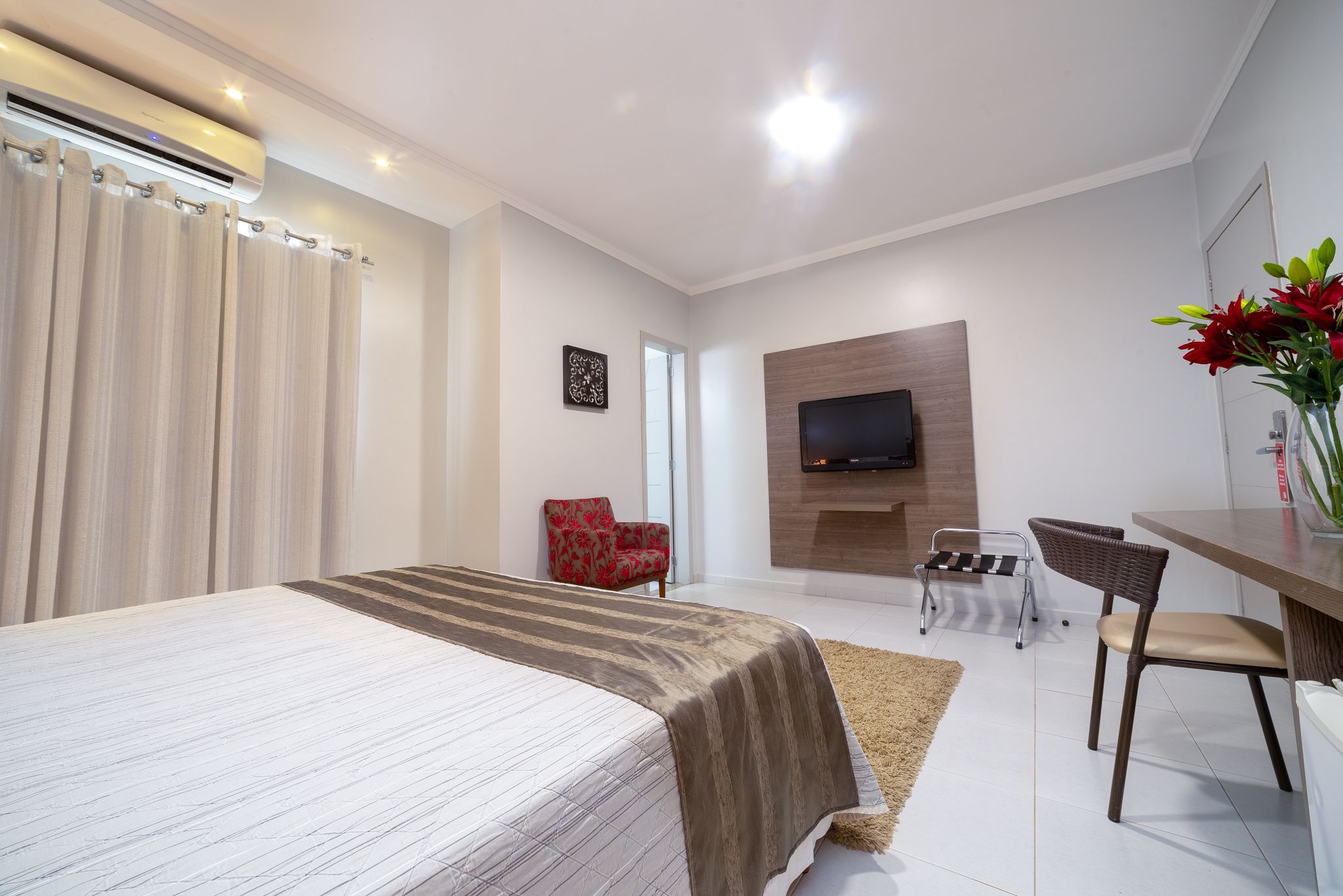 Een moderne hotelkamer met een groot bed, een bureau, een aan de muur bevestigde televisie en een rode stoel.